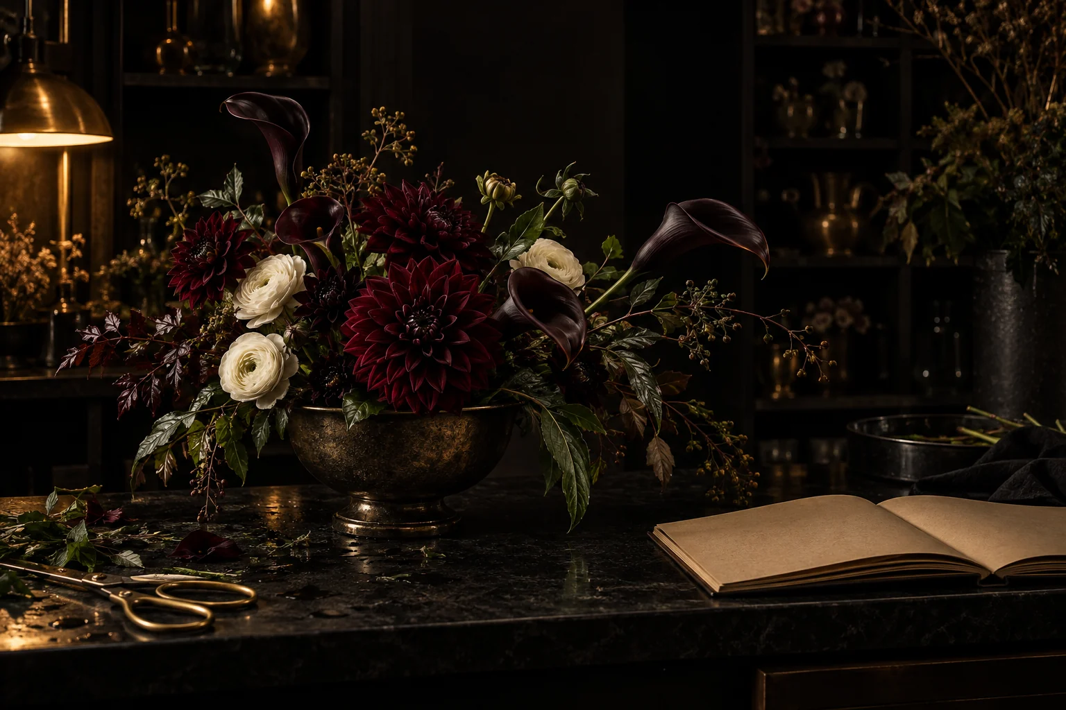 Finished burgundy arrangement in a bronze vessel on a dim florist workbench